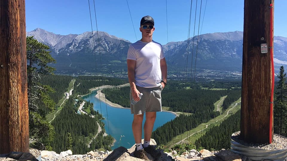 Harry standing in the sunshine on top of a mountain with mountains and blue sky in the background in Canada.